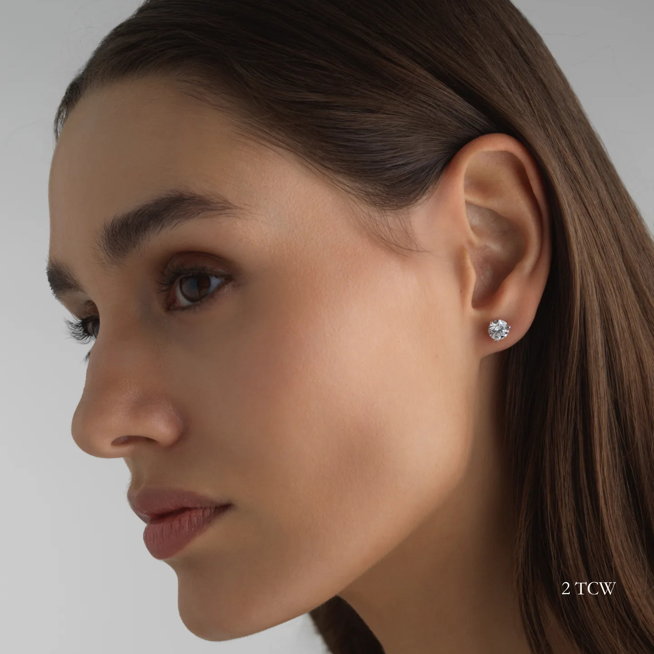 Close-up of a woman wearing a 2 total carat round diamond earring on a neutral background. Everyday sized lab diamond stud with modern setting for work or school.