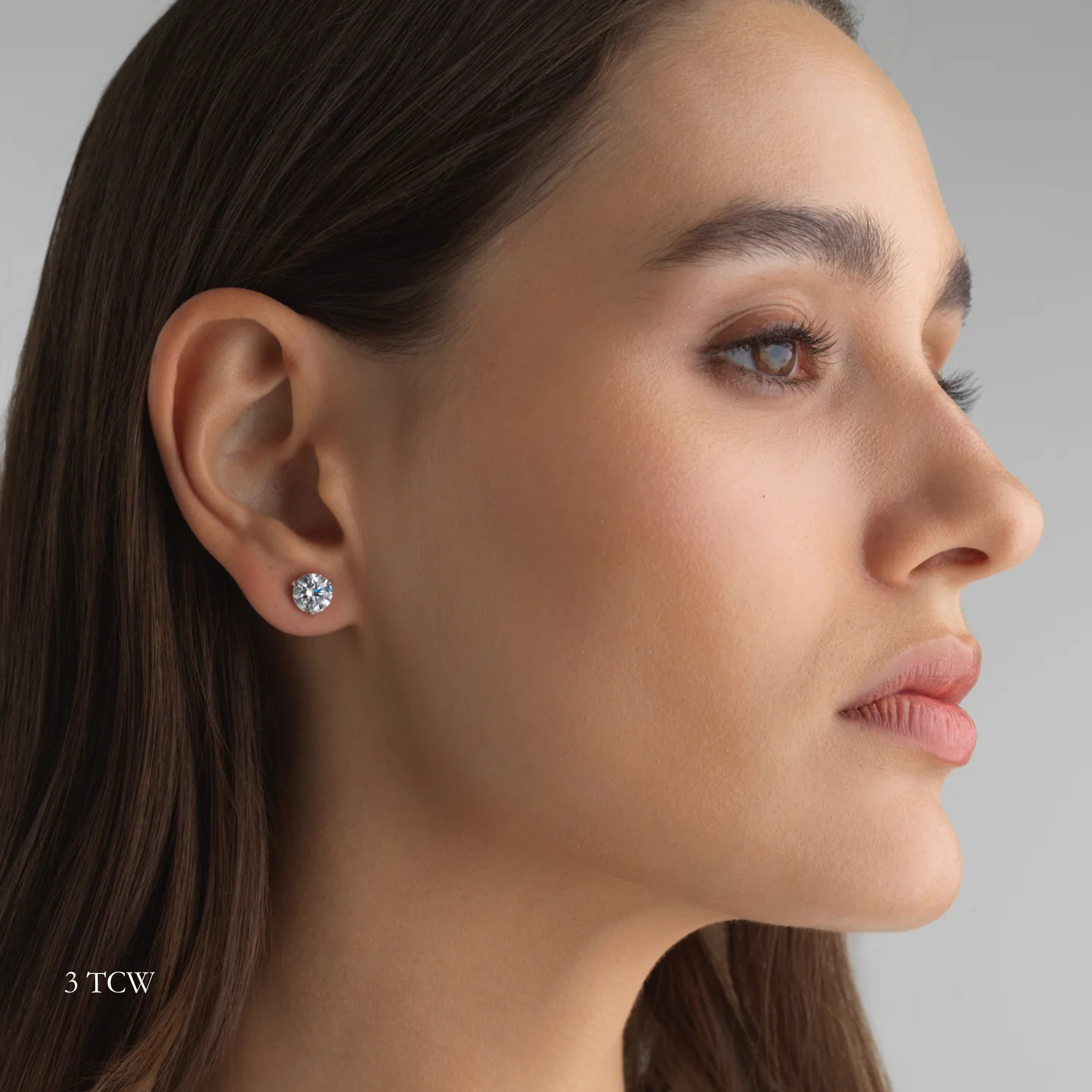 Close-up of a woman wearing a 3 total carat round diamond earring on a neutral background. Everyday sized lab diamond stud with modern setting in 14K gold for events of nights out. For a sophisticated woman with great taste. 