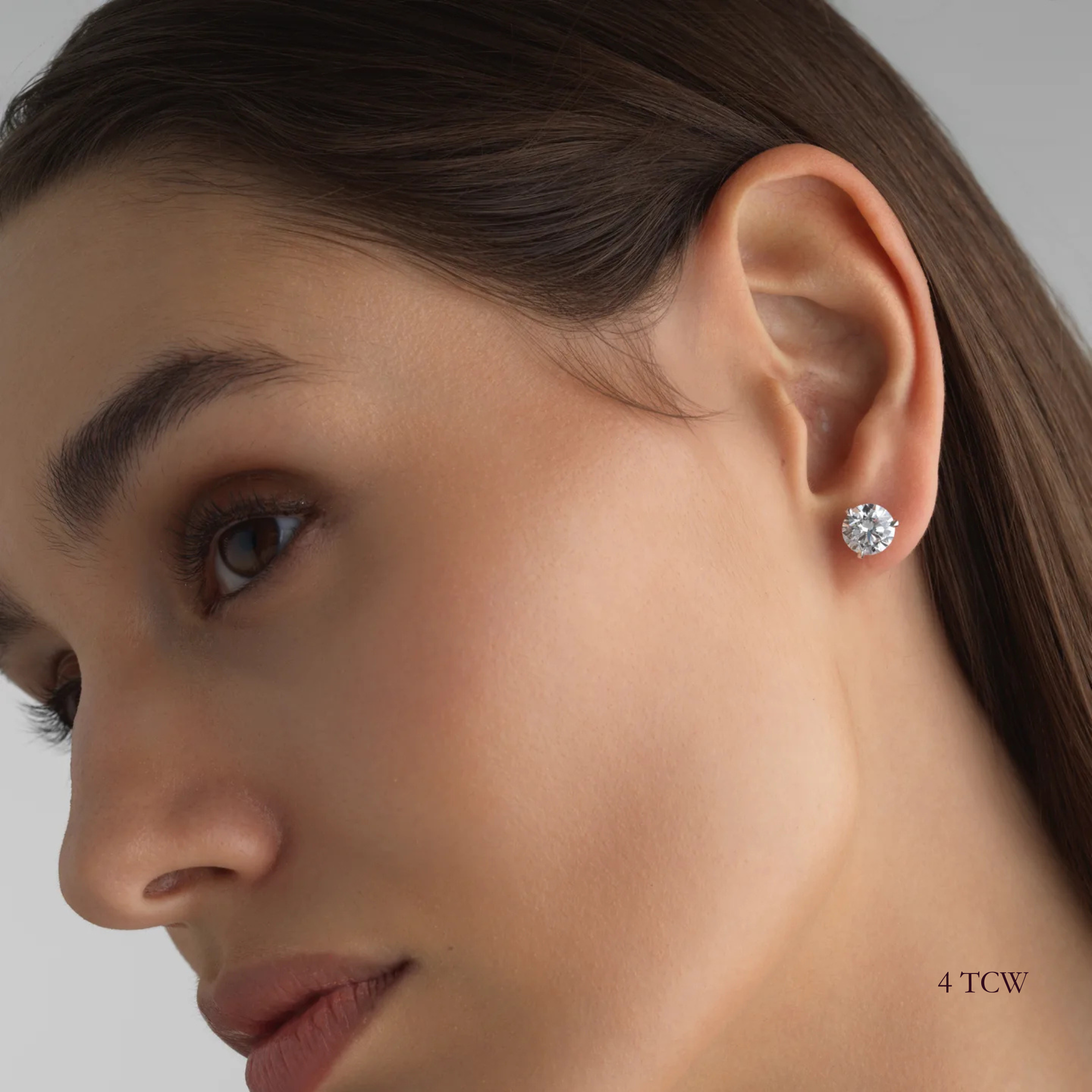 Close-up of a woman wearing a 4 total carat round diamond earring on a neutral background. Everyday sized lab diamond stud with modern setting in 14K gold for events of nights out. For a sophisticated woman with great taste. 