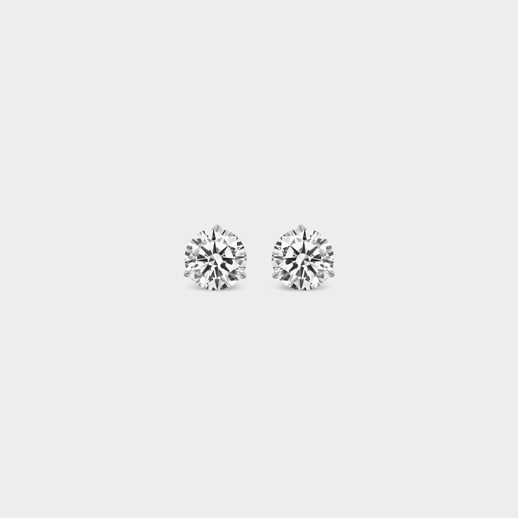 3 Prong Martini Diamond Studs. Close-up of a 0.5 TCW pair of round diamond earrings on a neutral background. Everyday sized lab diamond stud with modern setting in 14K gold perfect for building an ear stack.