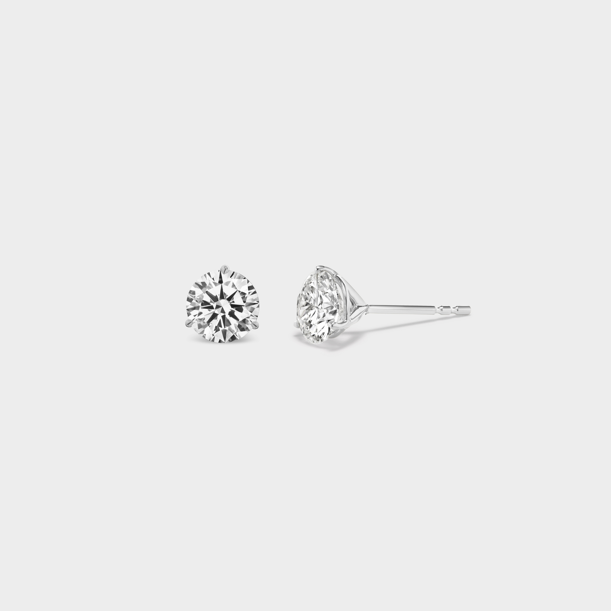 3 Prong Martini Diamond Studs. Close-up side view of a 0.5 TCW pair of round diamond earrings on a neutral background. Everyday sized lab diamond stud with modern setting in 14K gold perfect for building an ear stack.