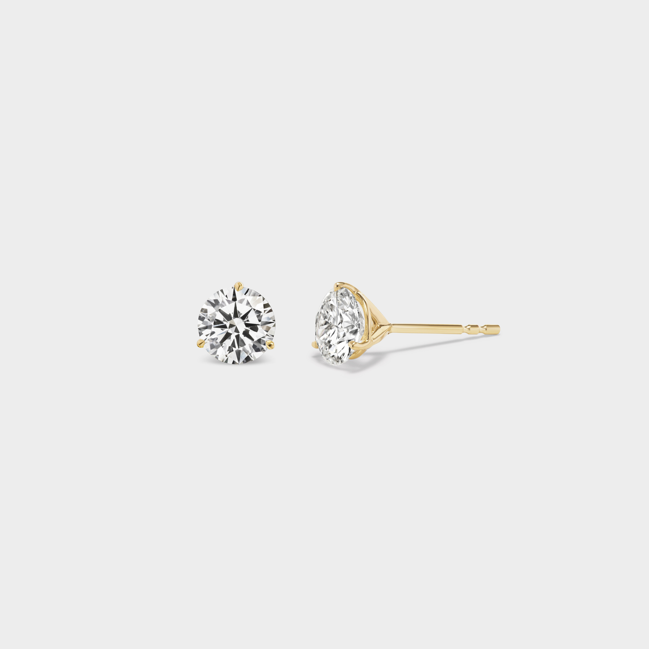 3 Prong Martini Diamond Studs. Close-up side view of a 0.5 TCW pair of round diamond earrings on a neutral background. Everyday sized lab diamond stud with modern setting in 14K gold perfect for building an ear stack.