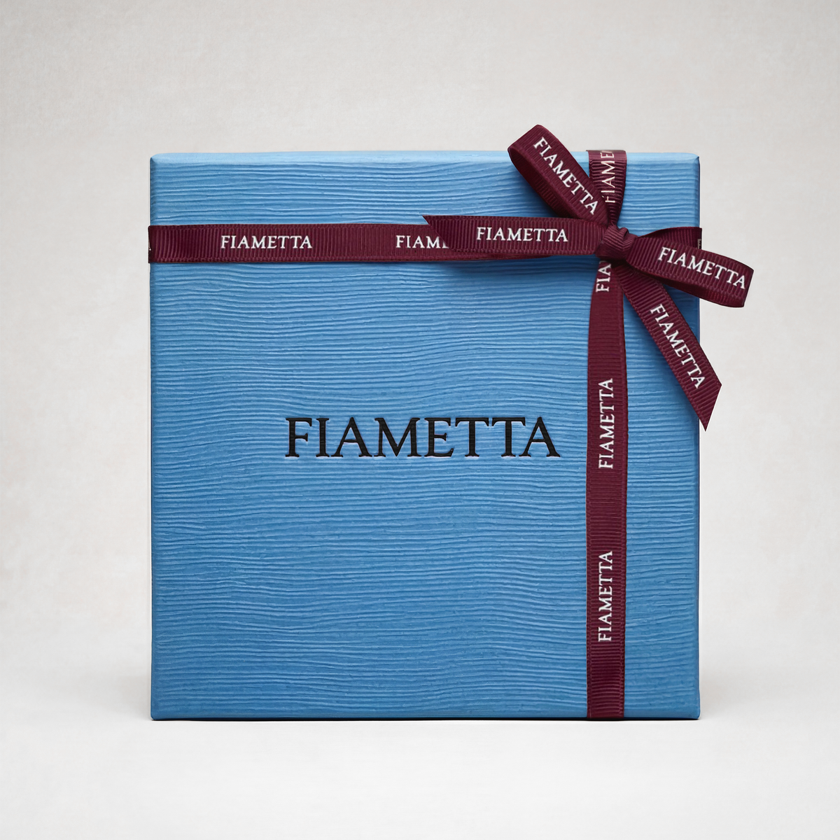 Blue Fiametta gift box with a textured finish, tied with a burgundy ribbon featuring the Fiametta logo.