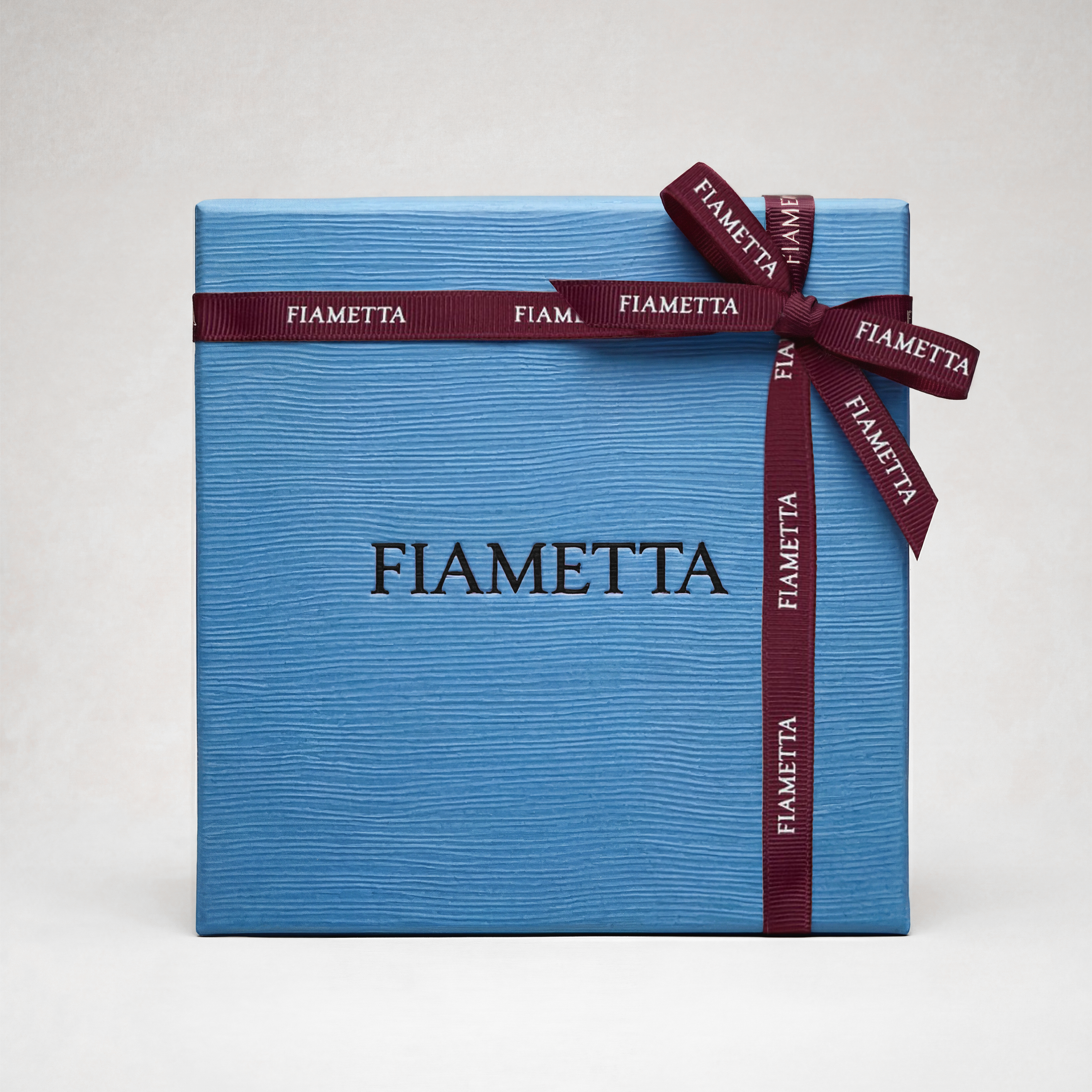 Blue Fiametta gift box with a textured finish, tied with a burgundy ribbon featuring the Fiametta logo.
