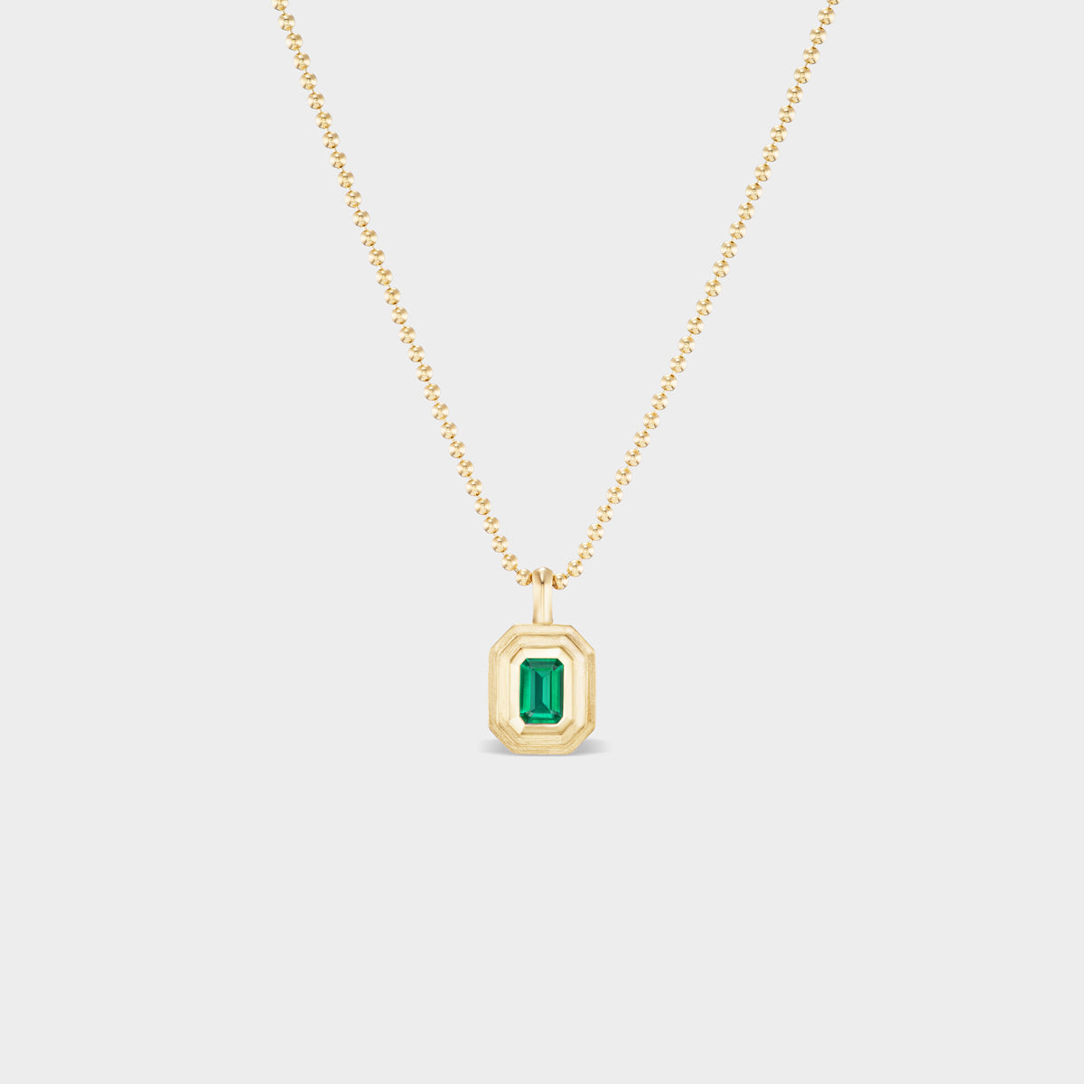 14K gold mini emerald bezel charm with triple-bezel setting on a delicate gold ball chain.