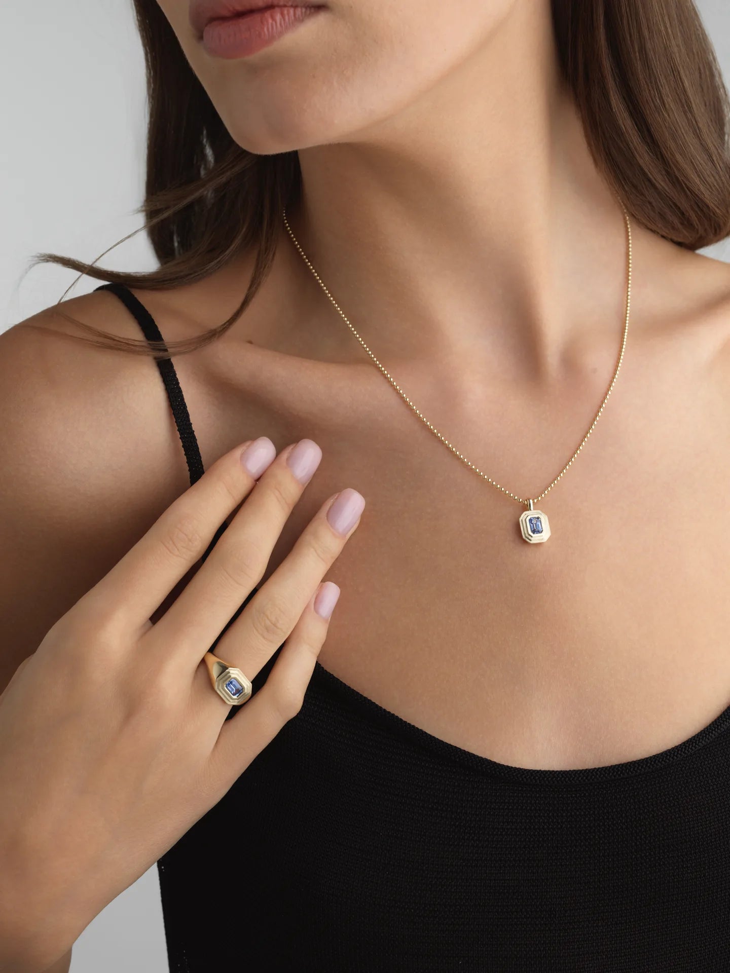 Woman wearing a 14k white gold 1.5mm ball chain necklace with a blue sapphire charm and matching ring.
