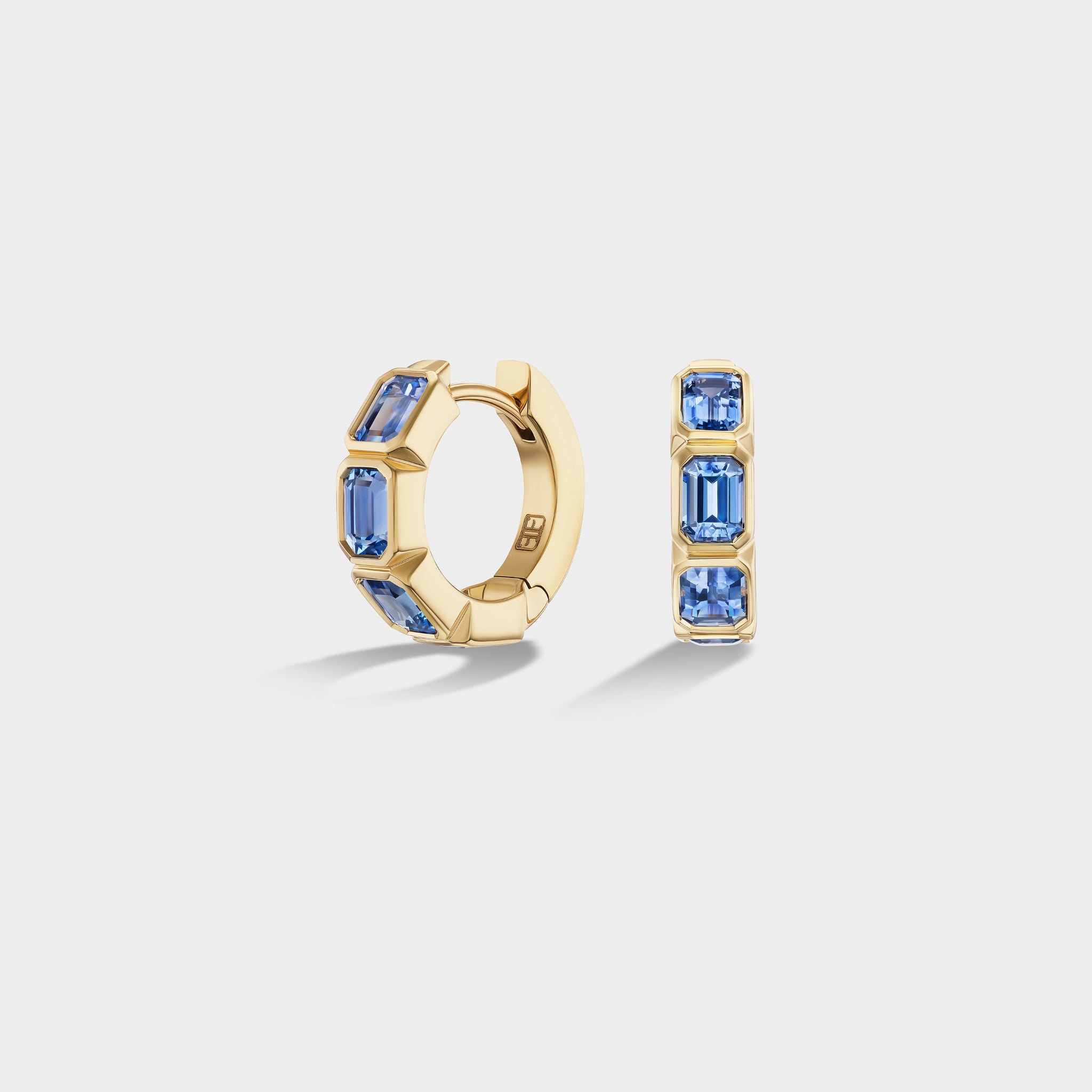 14K yellow gold mini huggie hoops with bezel-set emerald-cut natural blue sapphires, ideal for an ear stack.