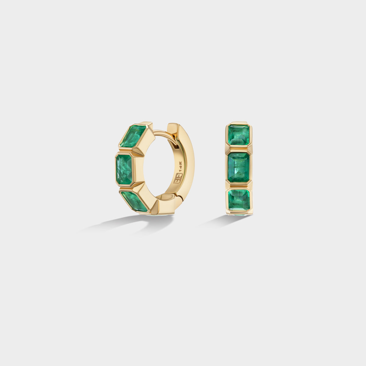 Mini 14K yellow gold huggie hoops with bezel-set emerald-cut natural emeralds, perfect for an ear stack.