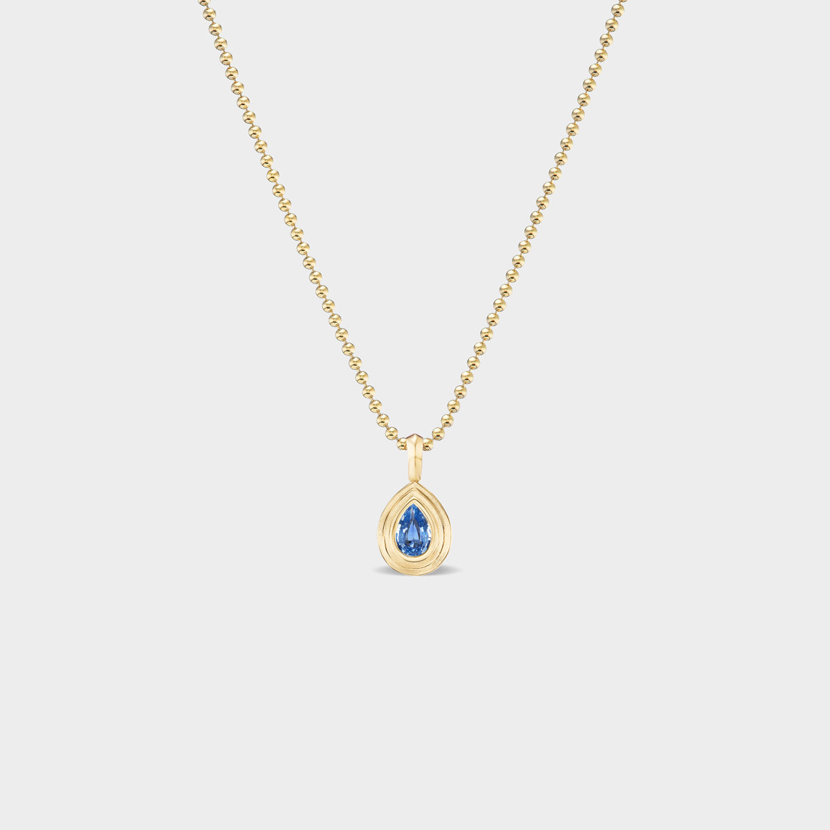 14K gold mini pear bezel charm with a natural blue sapphire, perfect for everyday wear.