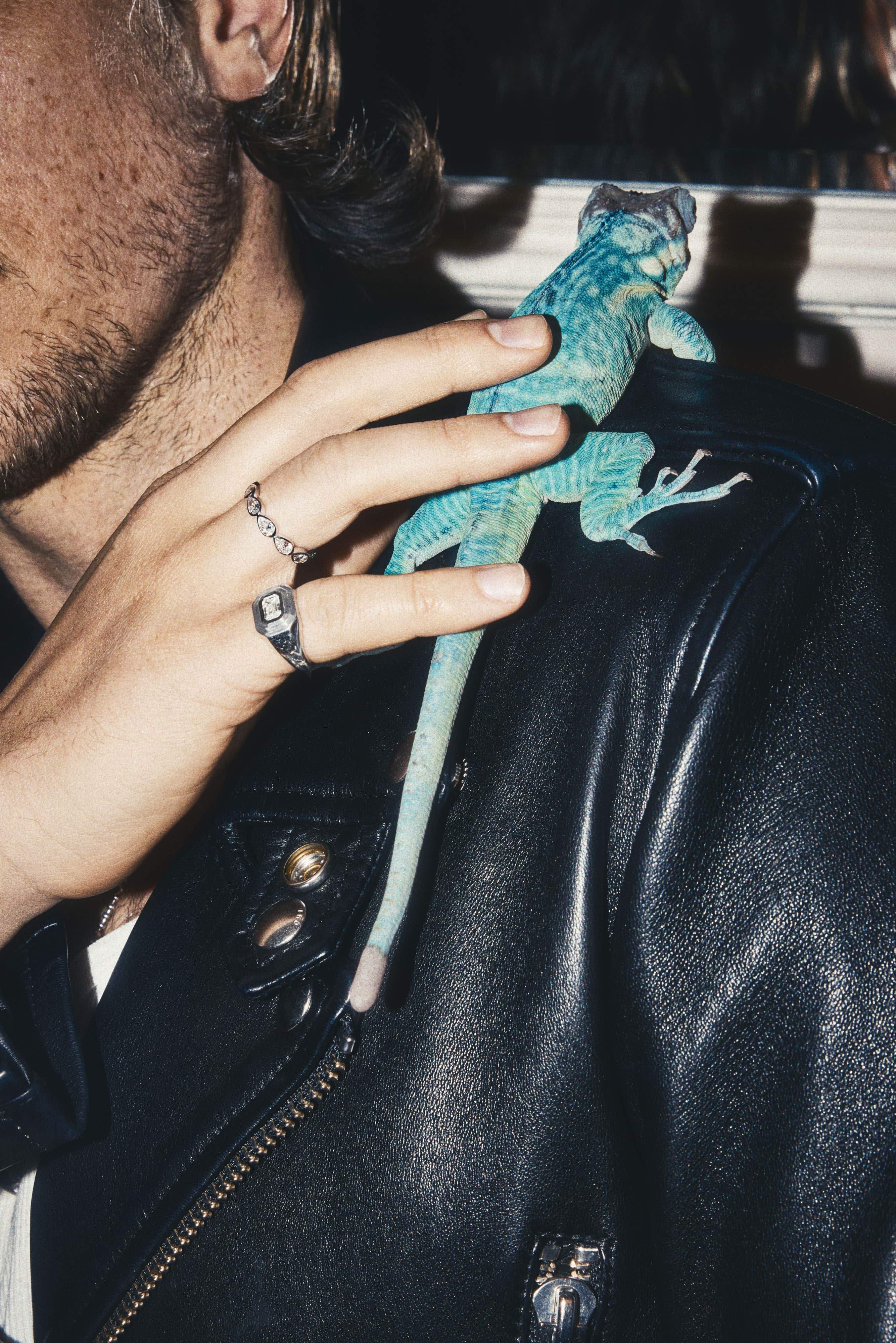 Man wearing a pear bezel eternity band and a square signet ring, with a blue lizard on his leather jacket.