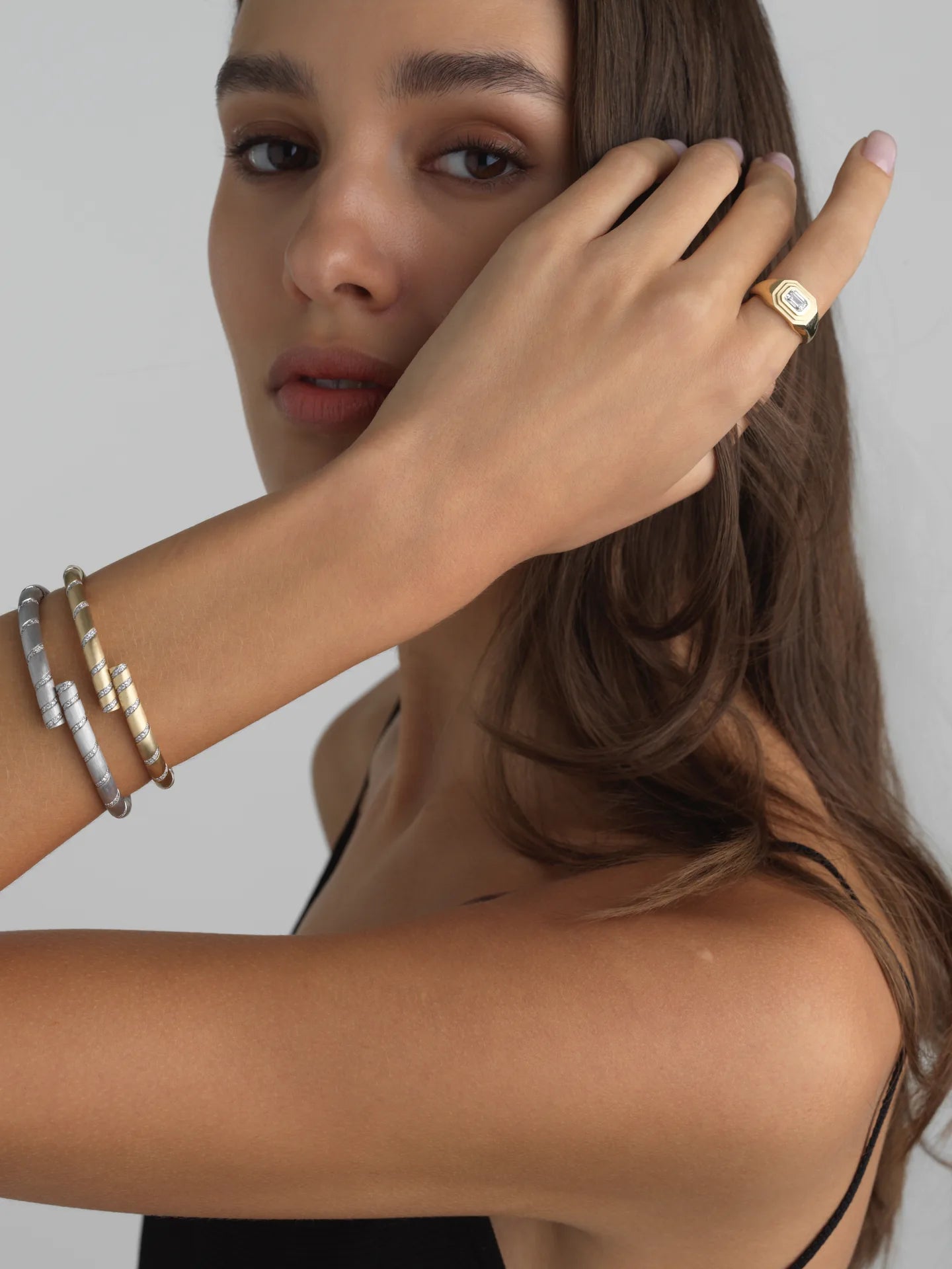 Model wearing a yellow gold emerald-cut lab diamond signet ring and two spiral bangles.