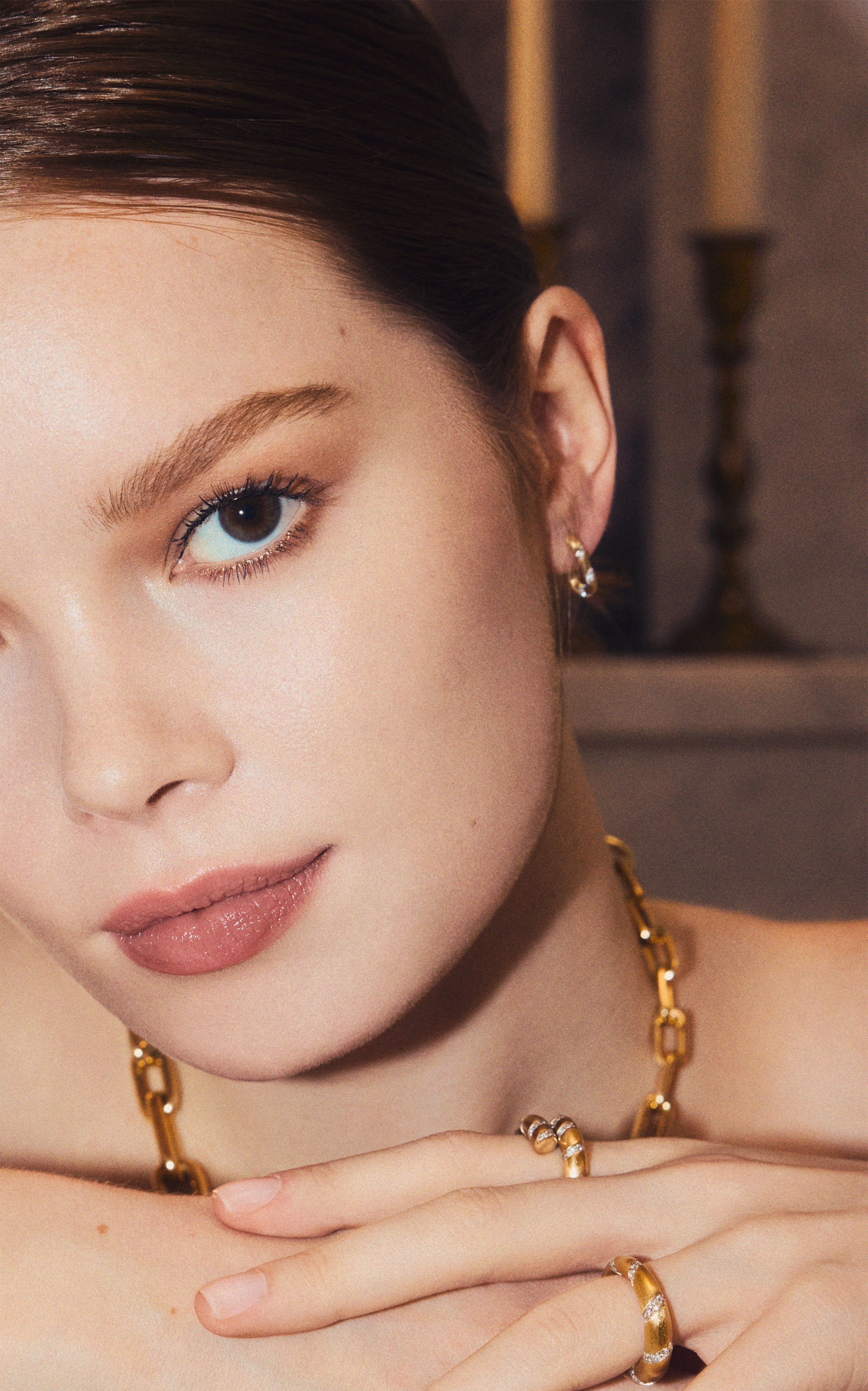 Woman wearing a yellow gold twist ring with lab-grown diamonds, a gold chain necklace, and stud earrings.