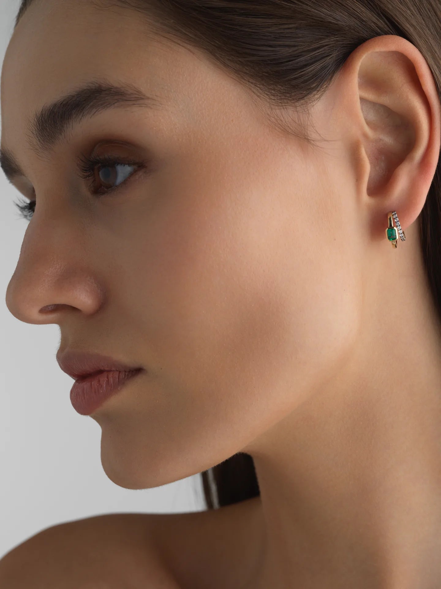 Model wearing Fiametta emerald-cut lab-grown diamond double hoop huggie earrings in 14k recycled yellow gold with pavé diamond accents and natural green emeralds. modern luxury fine jewelry combining old-world craftsmanship with ethical lab-grown diamonds. For the modern collector. An everyday style with a unique point of view.